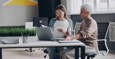 Twee zelfverzekerde vrouwen die technologieën gebruiken en communiceren terwijl ze samen op kantoor werken