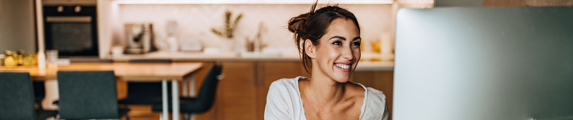 Een vrolijke vrouw die thuis aan het werk is achter de computer met op de achtergrond de keuken en eettafel