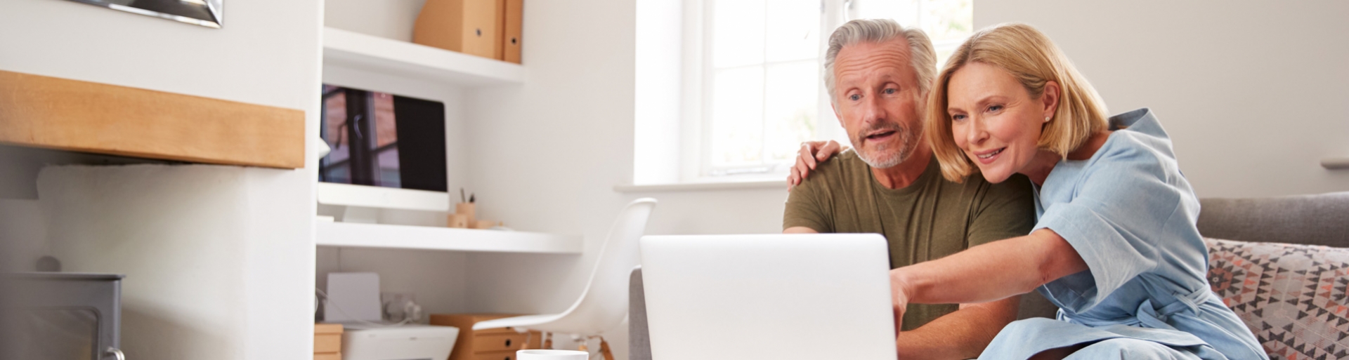 Ouder echtpaar zit thuis op de bank en gebruikt samen een laptop